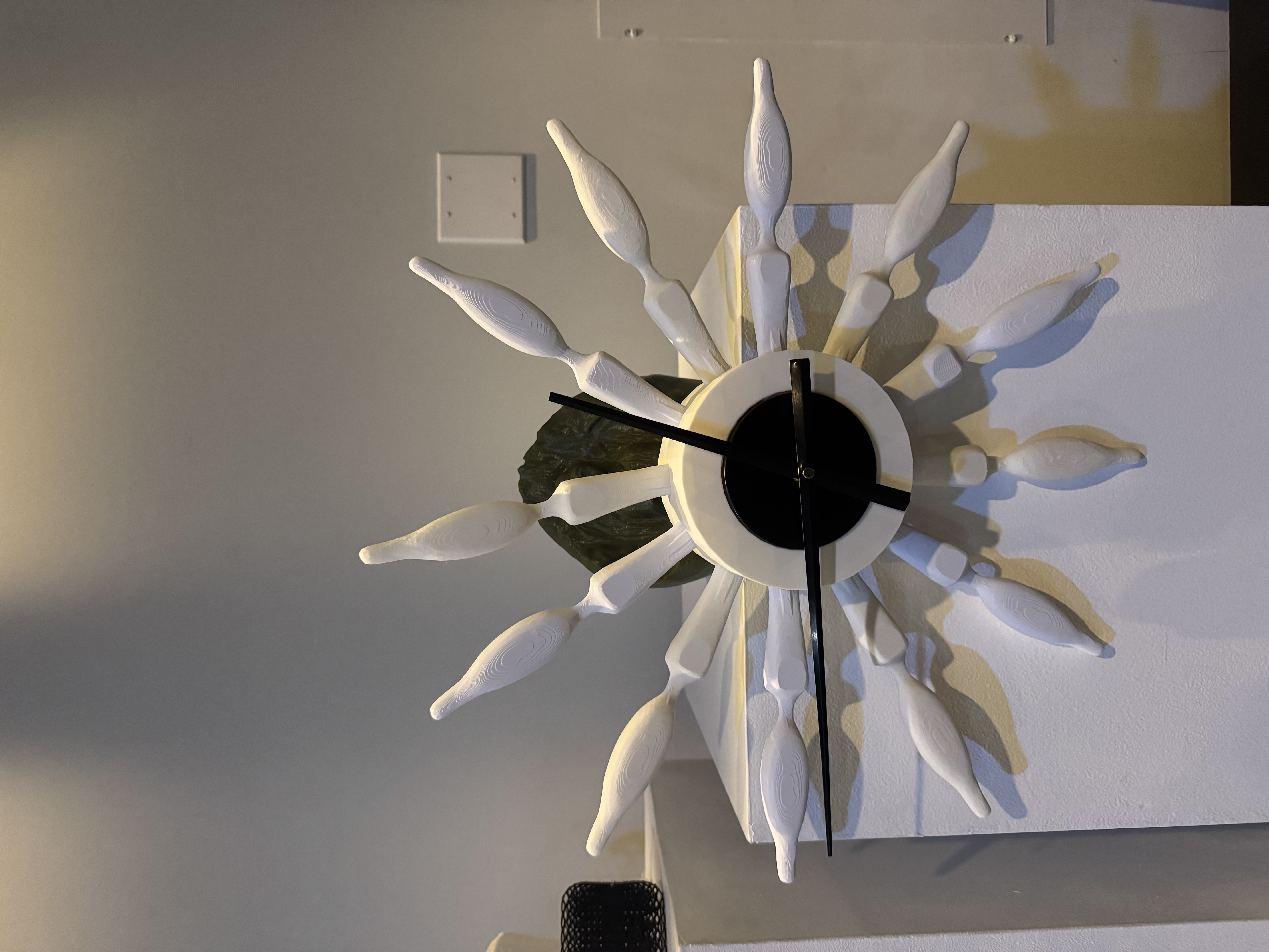 A 3D-printed seated Buddha figure anchored to a flat surface, cantilevering a printed housing that holds a working analog clock face out over the edge.